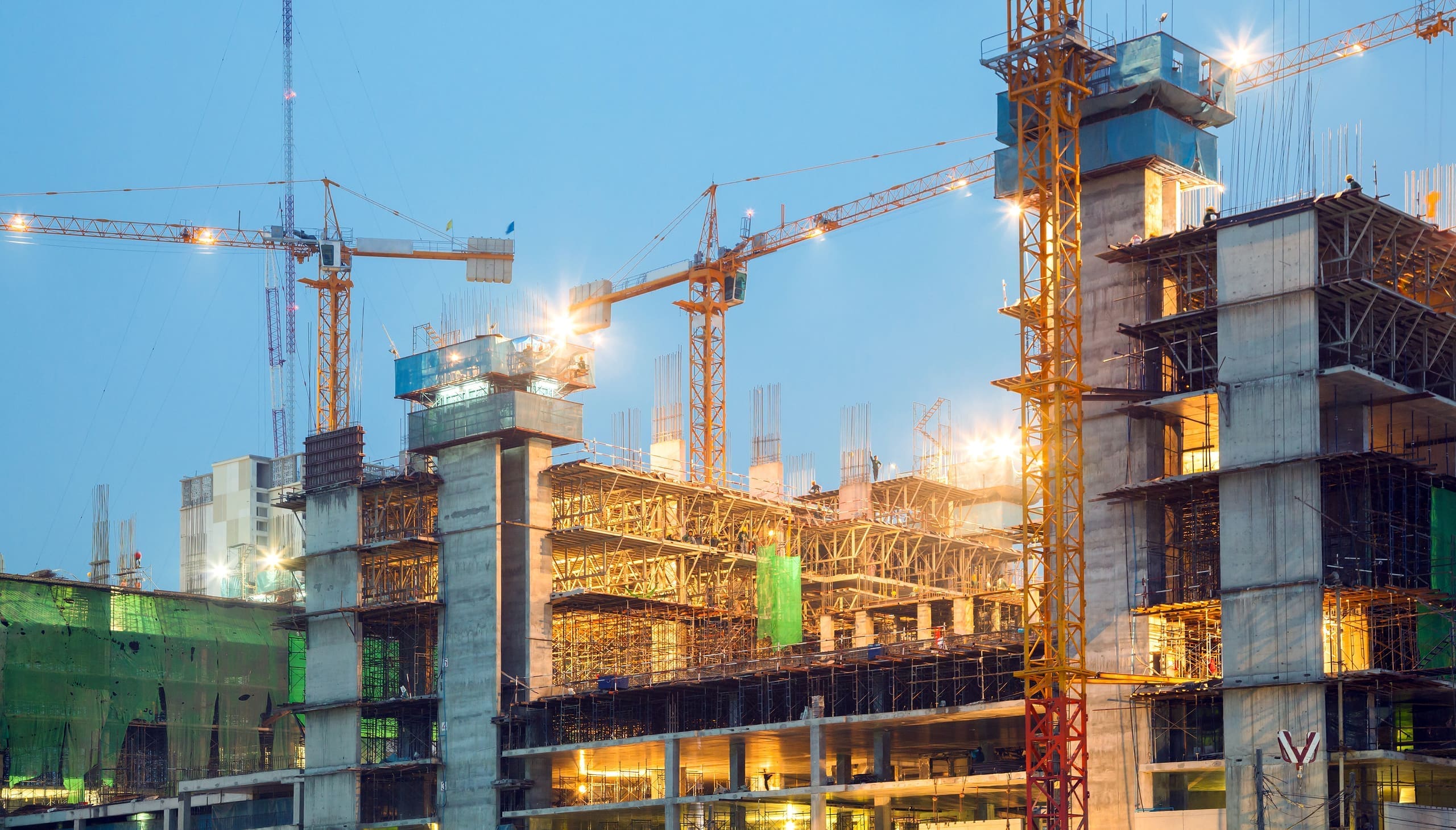 Tower cranes rising over a Metro Vancouver construction site at dusk